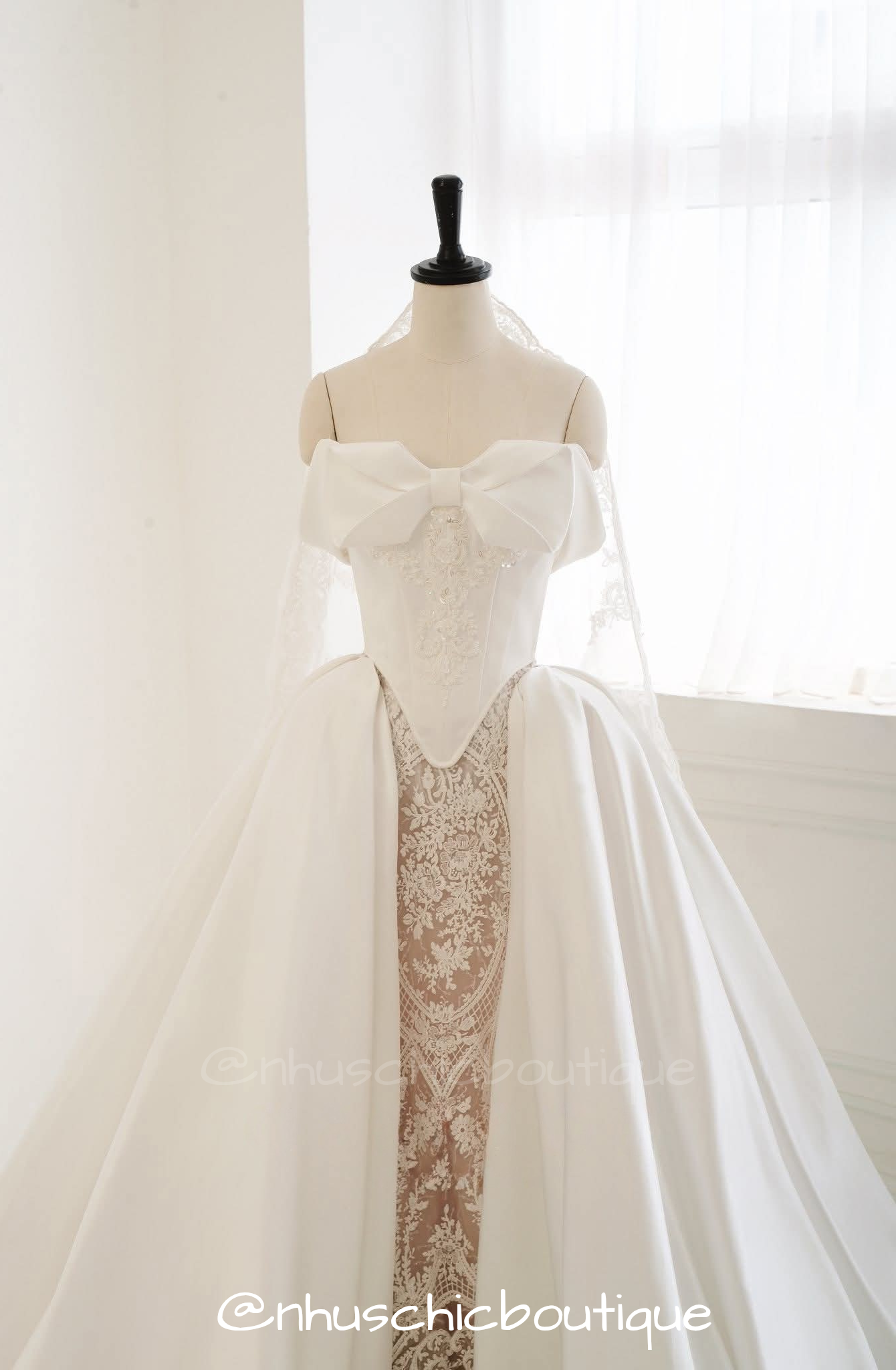4-in-1 convertible wedding dress by Nhuschicboutique featuring a structured white satin ball gown overskirt with a large statement bow bodice over an intricate lace underskirt.