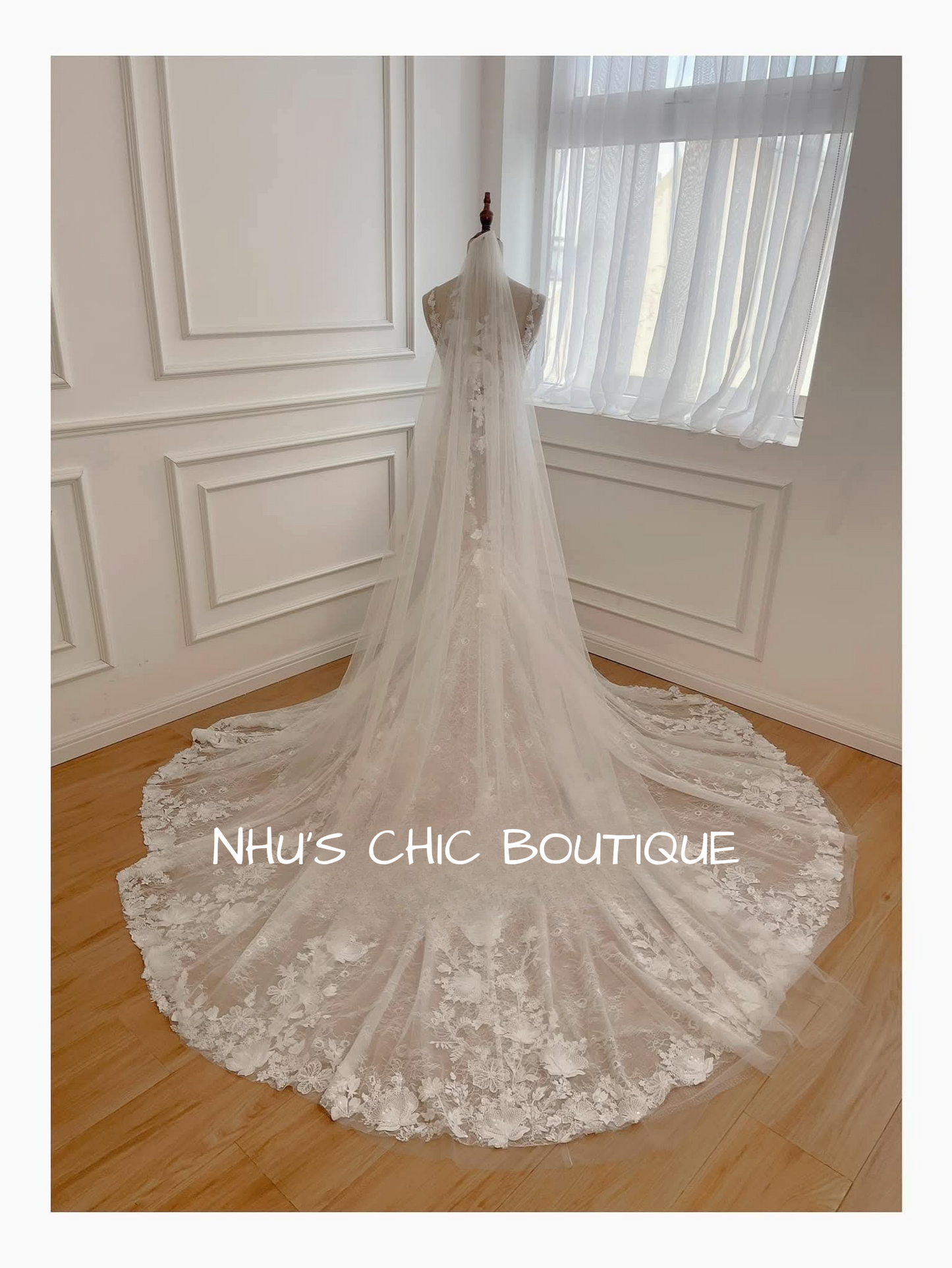 Lace wedding dress on a mannequin in a room with white walls and wooden floor.