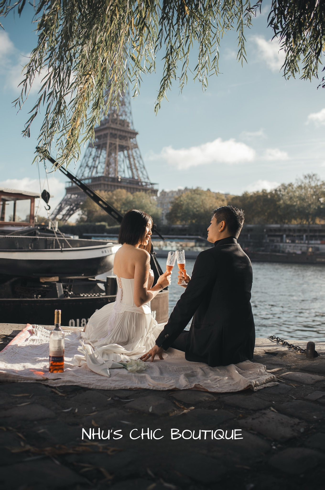 The bride and groom enjoying a Parisian picnic by the Seine, showcasing the back lace-up detail of the Genevieve pleated dress.