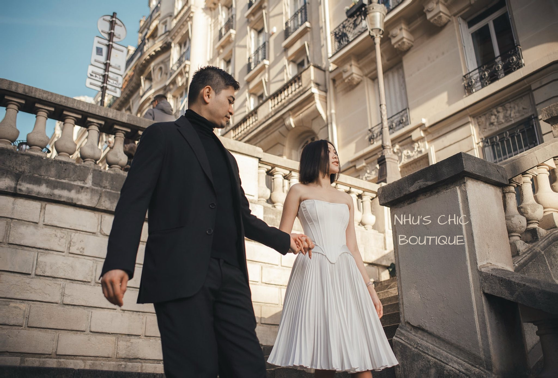 A dynamic shot of the bride and groom walking down stone steps in Paris, highlighting the movement of the Genevieve’s accordion pleated skirt.