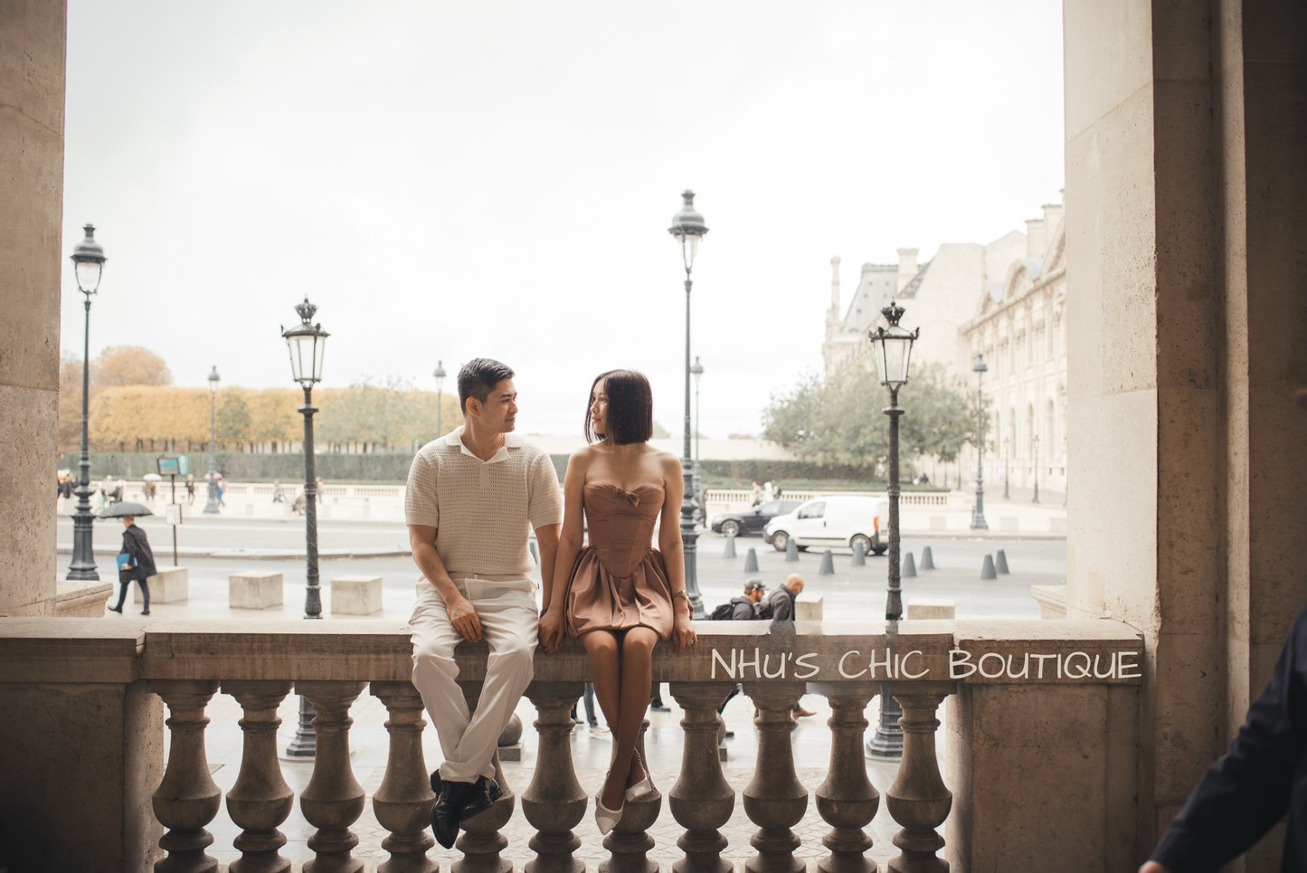A couple sitting on a stone railing in Paris, with the bride wearing the Chloe caramel mini dress and white mesh heels.