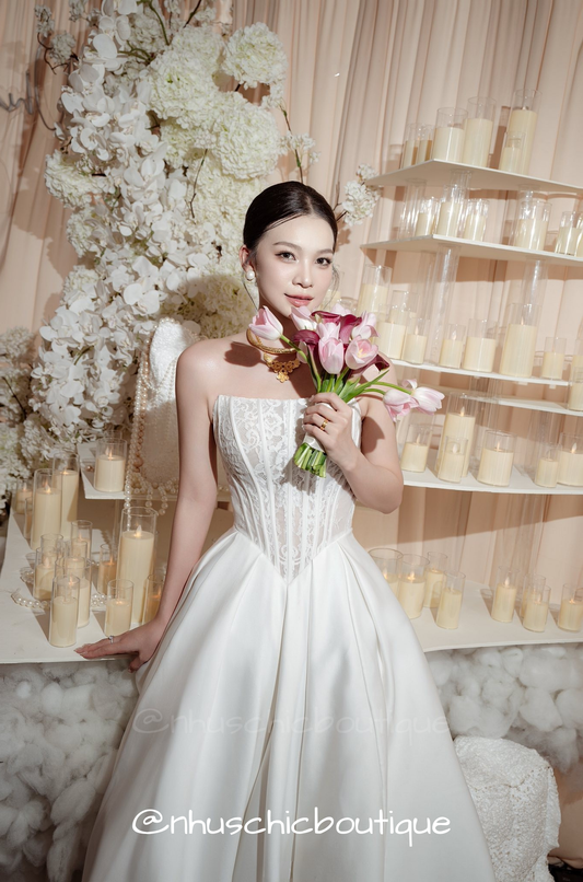 Front view of bride in strapless lace corset ballgown with a voluminous white satin skirt holding a pink tulip bouquet.