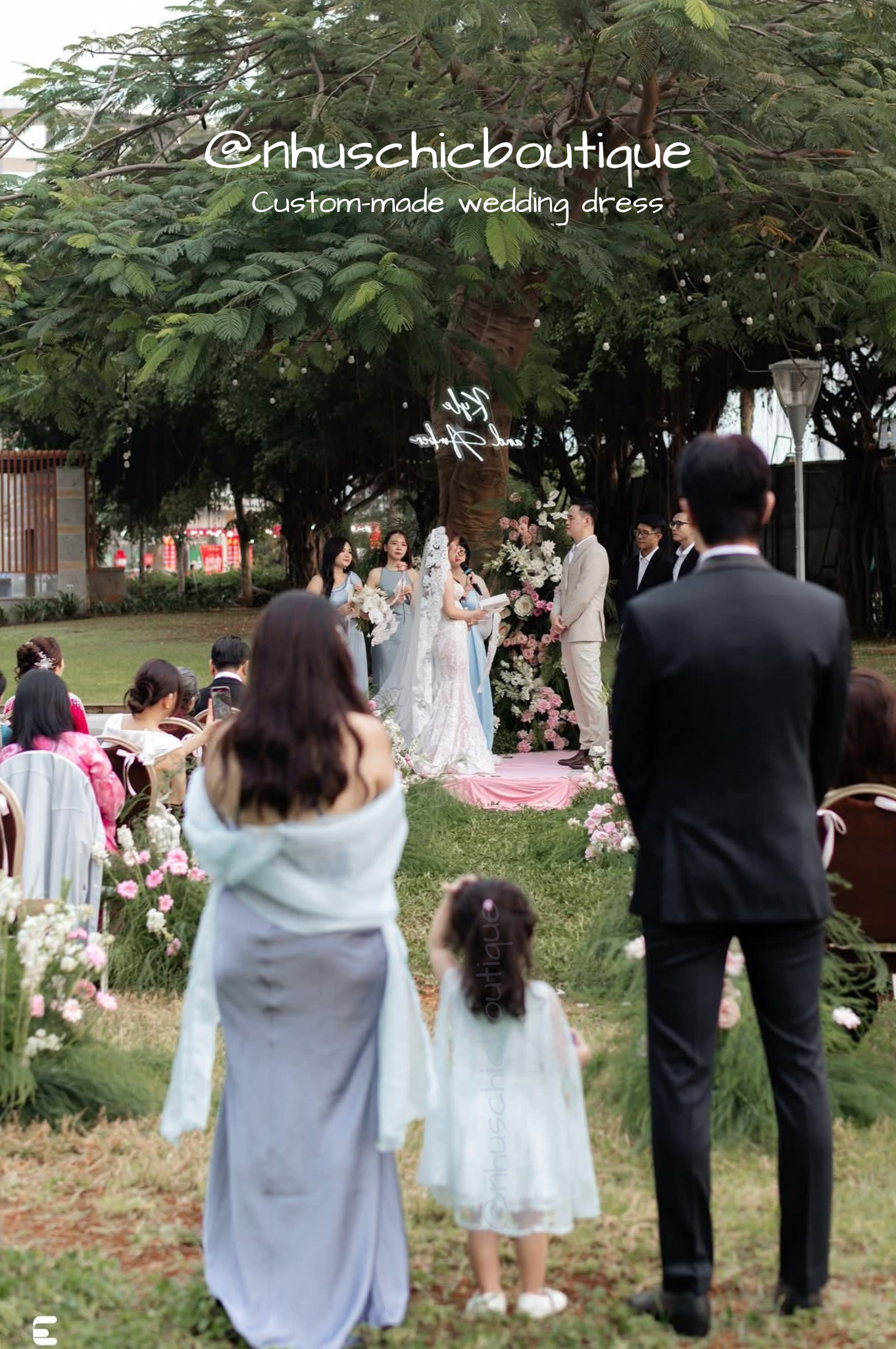 Full-length view of the bride and groom at an outdoor garden altar; the long lace train of the dress is visible on the grass.